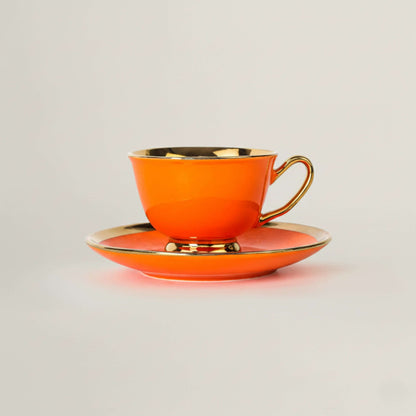 Orange porcelain tea cup and saucer with gold rim by Fleur de Lis
