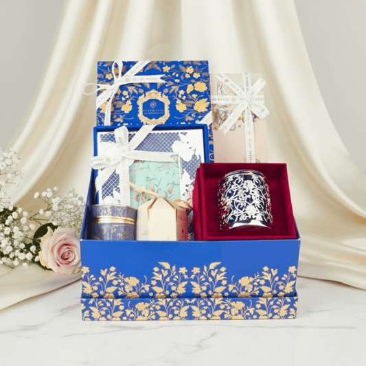 Premium Fleur de Lis gift hamper styled with soft draped fabric, showcasing luxury candle, gourmet confections, and handcrafted gift boxes in an elegant presentation.