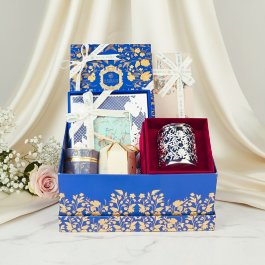 Premium Fleur de Lis gift hamper styled with soft draped fabric, showcasing luxury candle, gourmet confections, and handcrafted gift boxes in an elegant presentation.