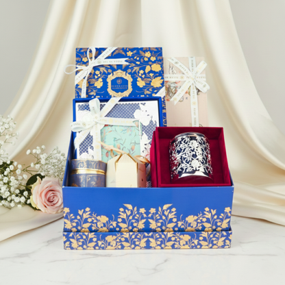 Premium Fleur de Lis gift hamper styled with soft draped fabric, showcasing luxury candle, gourmet confections, and handcrafted gift boxes in an elegant presentation.