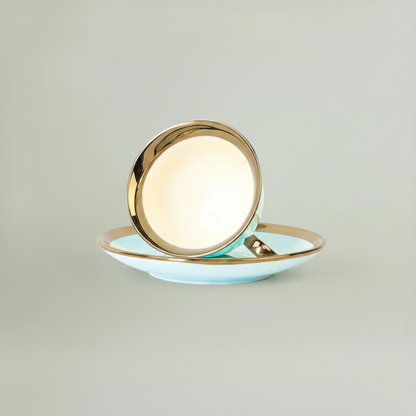 Close-up view of a sky blue ceramic cup resting on its saucer, highlighting the smooth glaze and gold-rim finish.