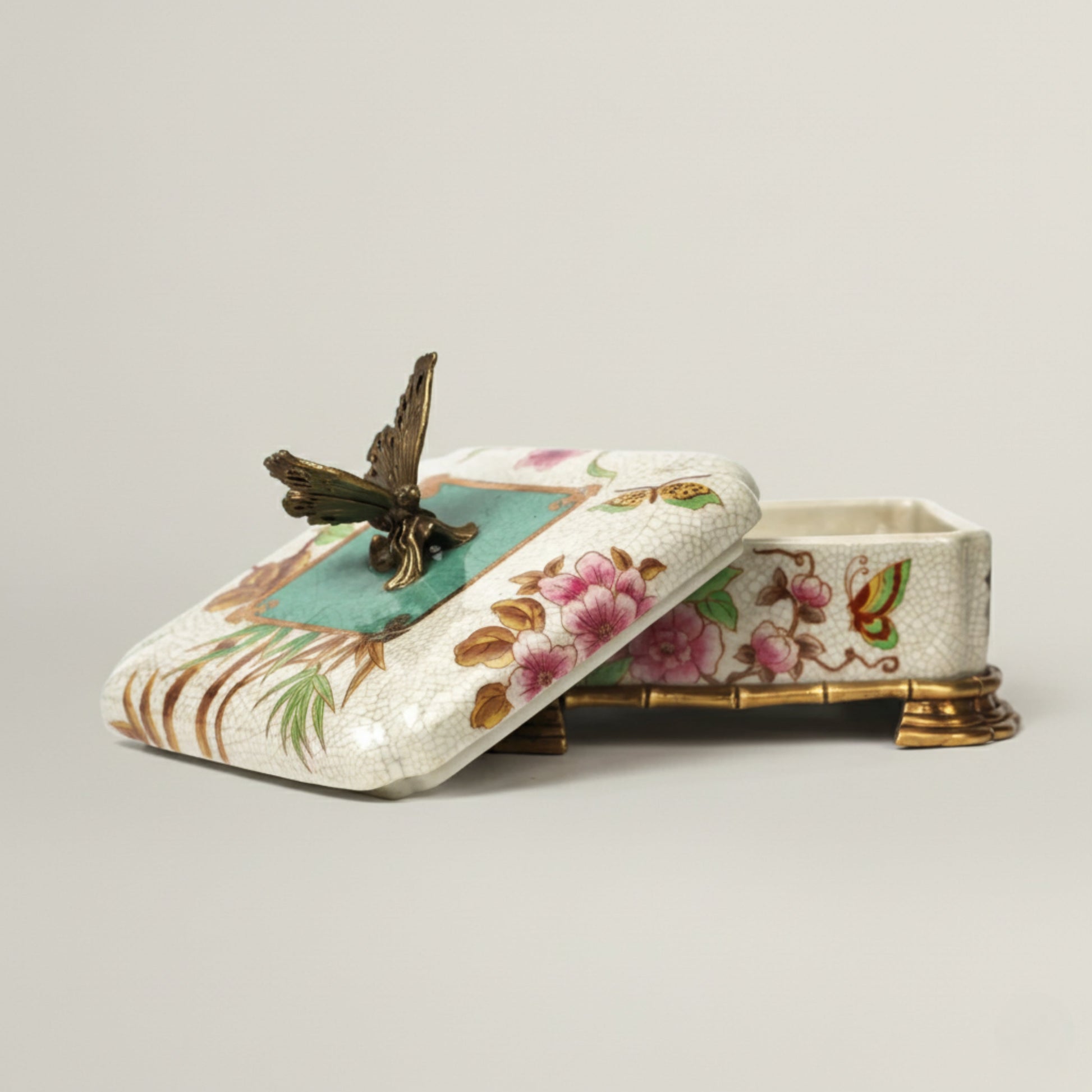 Hand-painted ceramic jewellery box with floral motifs, butterfly lid detail, and antique gold feet, designed for luxury home décor and gifting.