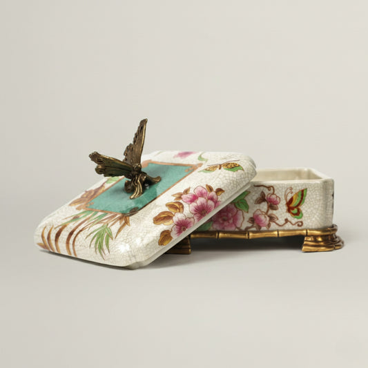 Hand-painted ceramic jewellery box with floral motifs, butterfly lid detail, and antique gold feet, designed for luxury home décor and gifting.