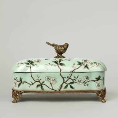 Mint green ceramic keepsake box with hand-painted floral branches, bird lid accent, and antique gold feet for elegant home décor.