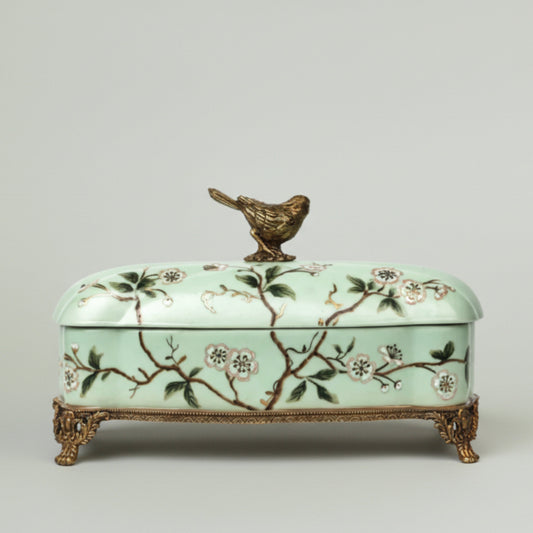 Mint green ceramic keepsake box with hand-painted floral branches, bird lid accent, and antique gold feet for elegant home décor.