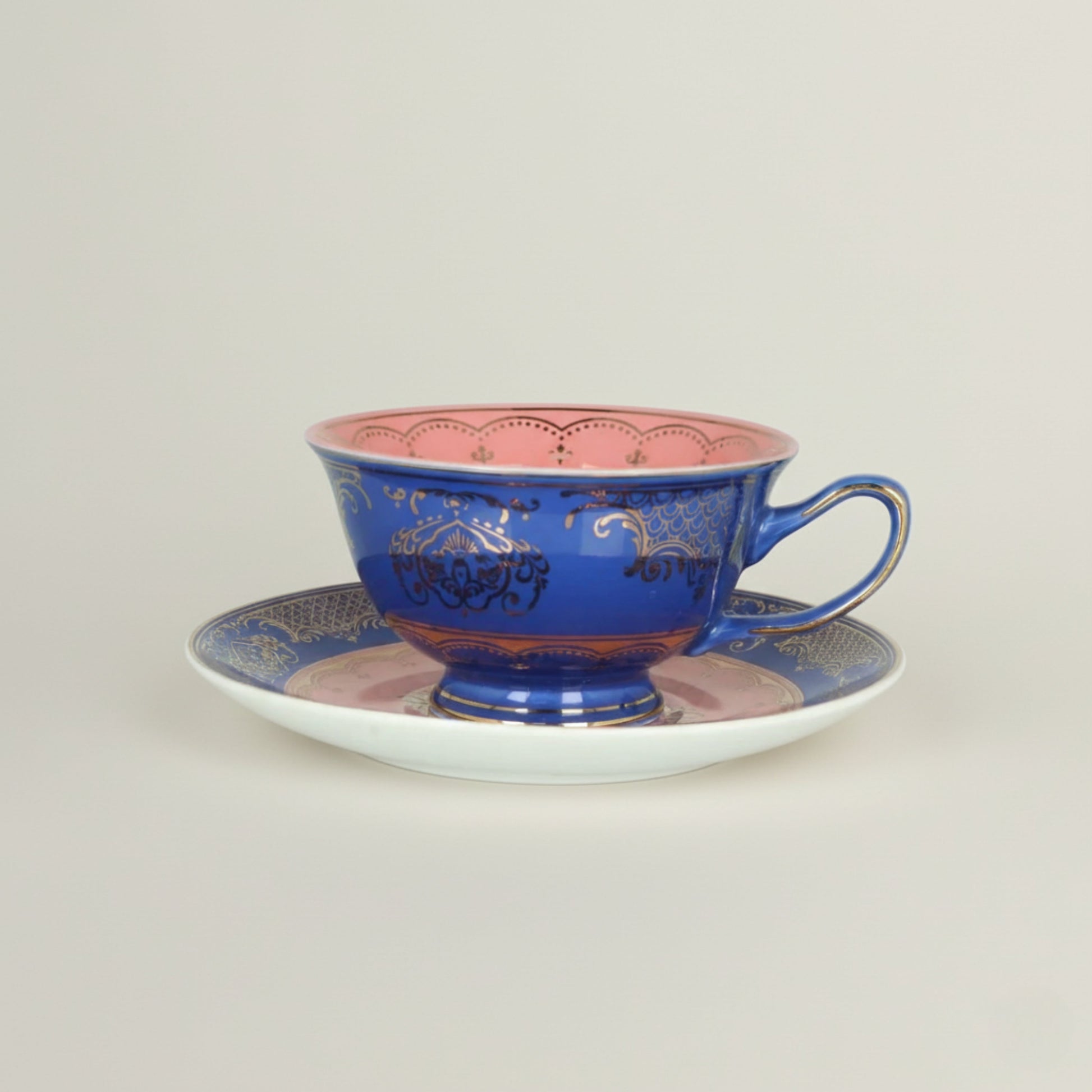 Royal blue ceramic coffee cup with soft pink interior and intricate gold detailing, paired with a matching decorative saucer.