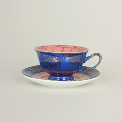 Royal blue ceramic coffee cup with soft pink interior and intricate gold detailing, paired with a matching decorative saucer.